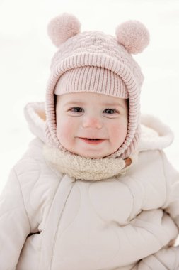 Kışlık kıyafetlerle sarılıp karda gülümseyen sevimli bir bebek.