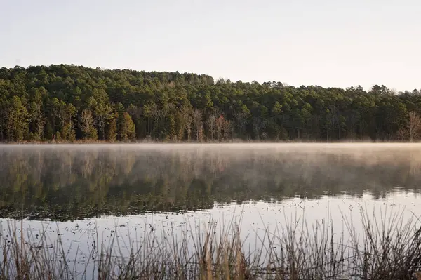 stock image Misty lake at dawn with forested hills in the background