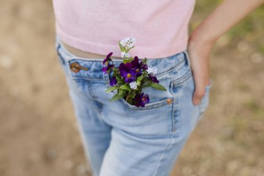 Cebi kır çiçekleriyle dolu, kot pantolonlu genç kıza yakın durun..