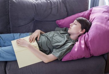 Kanepede uyuyan çocuk ve açık kitapla büyük yastık.