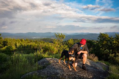 Adam köpeğini New Hampshire manzaralı bir bakış açısıyla okşuyor.