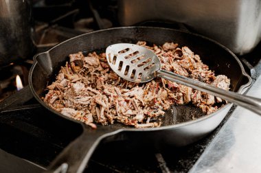 skillet of pulled meat with giant metal spoon sitting on stove top clipart