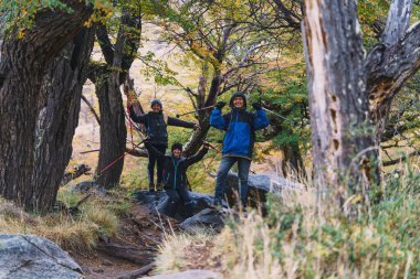 Üç kişi ormanda fotoğraf çektirmek için poz veriyor.