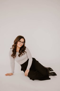 Genç İspanyol kadın yerde oturuyor, gülümsüyor, beyaz arka planı var.