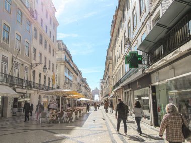 Güneşli Avrupa caddelerinde insanlar, kafeler ve tarihi binalar var.