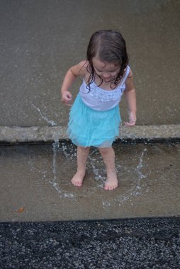 Yağmur fırtınası sırasında su birikintisine sıçrayan genç kız