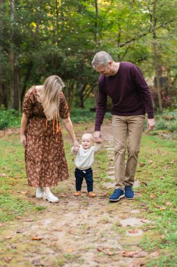 Ebeveynler küçük çocuğa gülümsüyor ve yürürken ellerini tutuyorlar..