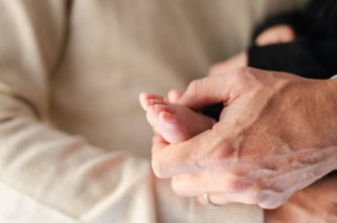 Yeni doğmuş bir bebeğin küçük ayağını nazikçe tutan eller..