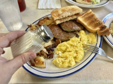 Kahvaltı tabağının üzerine yumurta, sosis ve tost serpiyorum.