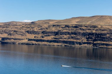 Arka planda engebeli tepelerle gölde tekne gezintisi..