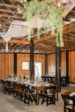 Ahşap masalar ve sicim lambalarıyla kapalı bir düğün resepsiyonu.