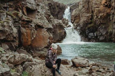 Woman sitting on rocks an watching Tofufoss waterfall, Iceland clipart