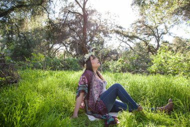 Ormanda çimenlerde oturan, taç takan bir kadın.