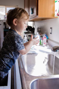Bebek gün ışığında mutfak lavabosunda ellerini yıkıyor.