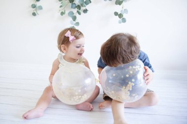 İki çocuk yerde oturmuş balonlarla oynuyorlar.