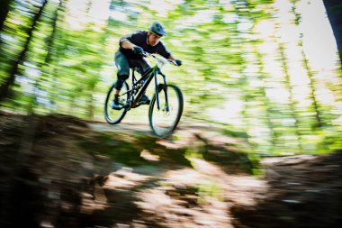 Dağ bisikletçisi ormanda yokuş aşağı koşuyor.
