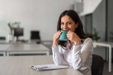 Elinde kahveyle gülümseyen bir ofis çalışanı.