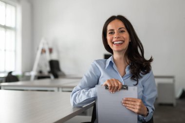 Genç ve neşeli bir çalışan elinde belgelerle masasında.