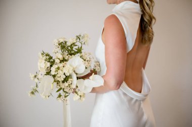 Sırtsız gelinlik giymiş, elinde beyaz bir buket tutan gelin.