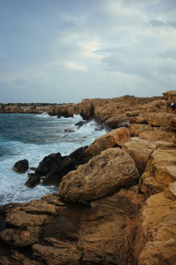 Bulutlu bir gökyüzünün altında dalgalı kıyı şeridi.