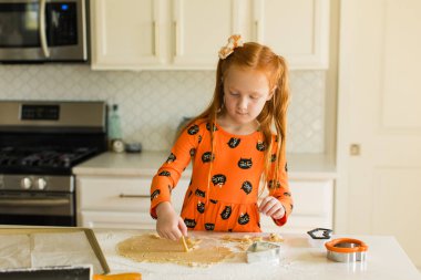 Kızıl saçlı, turuncu elbiseli Cadılar Bayramı şekerli kurabiyeler yapıyor.