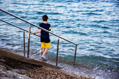 Çocuk merdivenlerden denize iniyor.