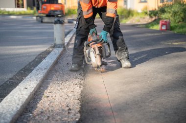 İnşaat işçisi yolda asfaltı dairesel testere ile keser.