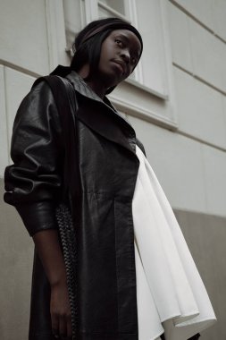 Açık havada genç siyah bir kadın. Siyah ceket giyiyor.