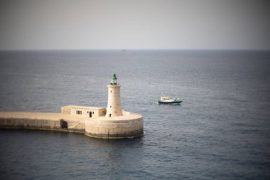 Valletta, Malta 'da yeşil bir deniz fenerinin yanından geçen küçük bir pilot teknesi..