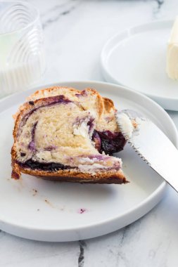 Beyaz bir tabakta bıçakla yaban mersini krem peynirli babka dilimi.