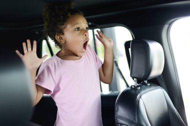 Child in a car expressing surprise or excitement with hands rais clipart