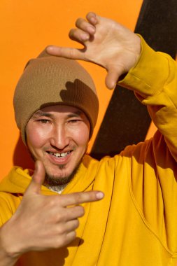 Sarı kapüşonlu şık bir adam elleriyle jest yapıyor.
