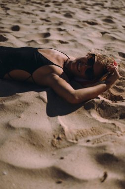 Mayo giymiş bir kadın kumlu sahilde dinleniyor..