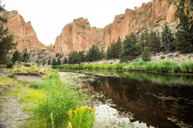 Smith Rock State Parkı 'nda yükselen kızıl kayalıkları yansıtan sakin nehir..