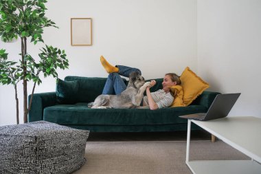 Kadın evinde köpeğiyle kanepede yatıyor.