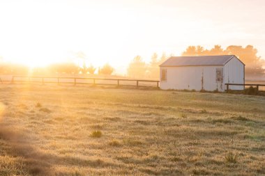 Sabahın erken saatlerinde güneşli bir arazide küçük bir kır kulübesi.