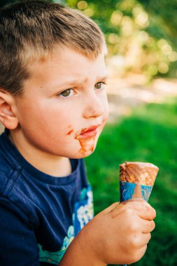 A young boy with a chocolate-stained face holding a melting ice cream clipart