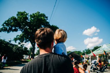 Omzunda küçük bir çocuk taşıyan bir adam, arkadan bakmış.