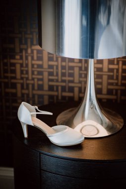 Gelin beyaz ayakkabısı modern lambanın altında, zarif düğün ayrıntıları.