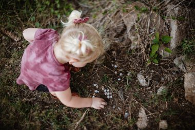 Çömelmiş, çamurdaki salyangoz kabuğu koleksiyonuna bakıyor.
