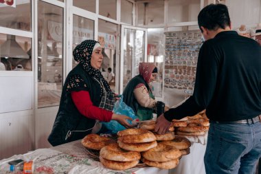 Kırmızı gömlekli bir kadın markette ekmek satıyor.