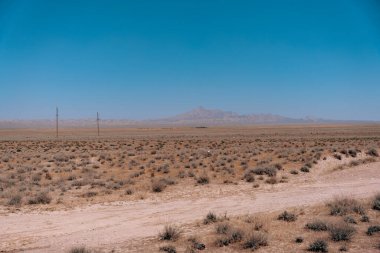 Arka planda mavi gökyüzü olan çorak bir çöl manzarası.