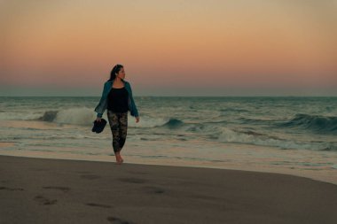 Woman walks barefoot along the seashore to feel the water on her feet. clipart