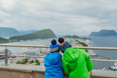 Two boys in winter gear overlook the scenic town of lesund, Norway   clipart