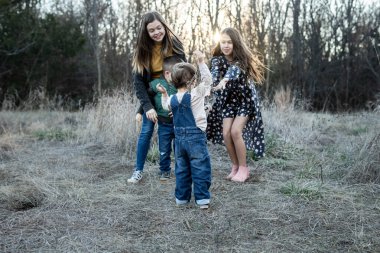 Çimenli alanda oynayan kardeşler ağaçların arasından süzülen güneş ışığı