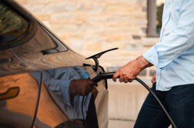 Dışarıdaki elektrikli araca EV şarj cihazı takan adama yaklaş..