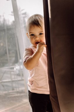 Playful toddler girl hiding behind sliding door curtain clipart