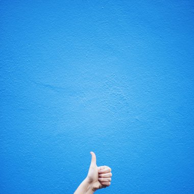 El, mavi duvara karşı baş parmak işareti gösteriyor.