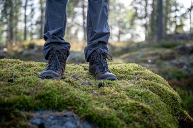 Ormanda yeşil yosunların üzerinde duran yürüyüş botlarının yakın çekimi.
