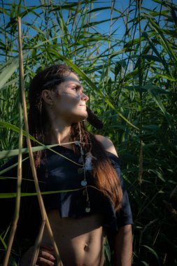 Amazon gibi giyinmiş genç bir kadın çalılıklarda poz veriyor.